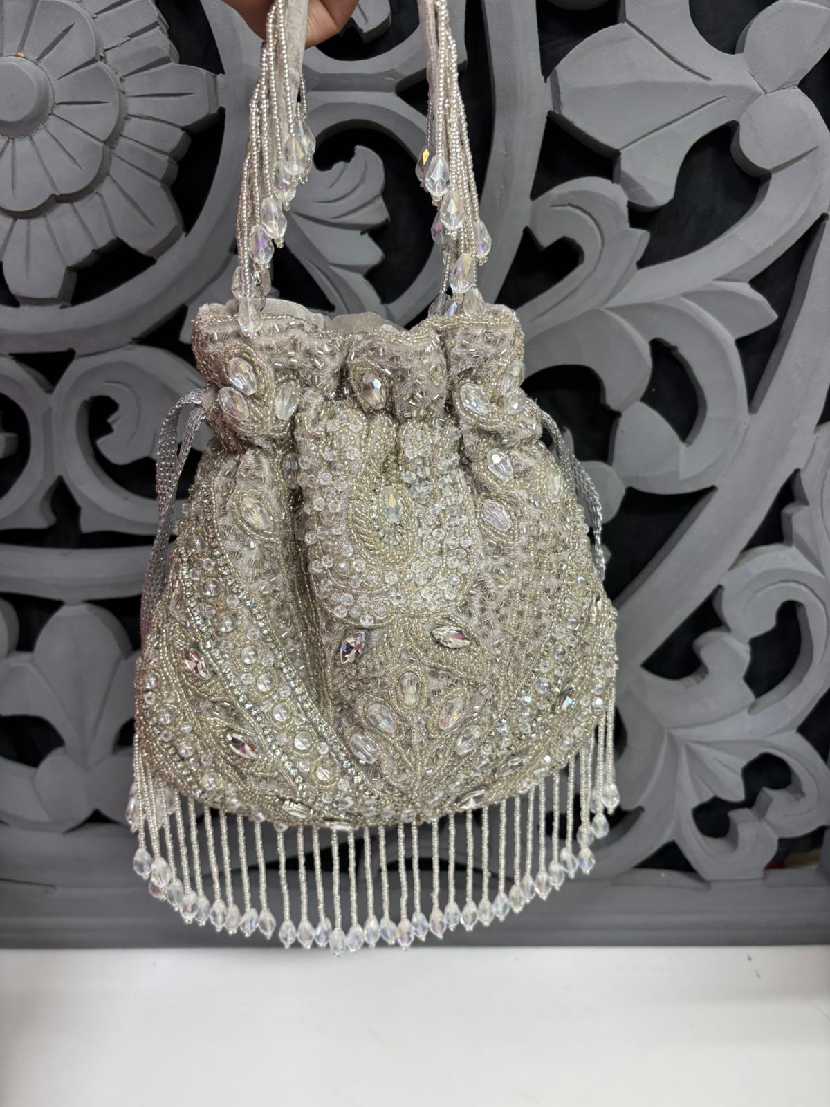 Decorative handbag with beads and fringes against an ornate decorative wall.