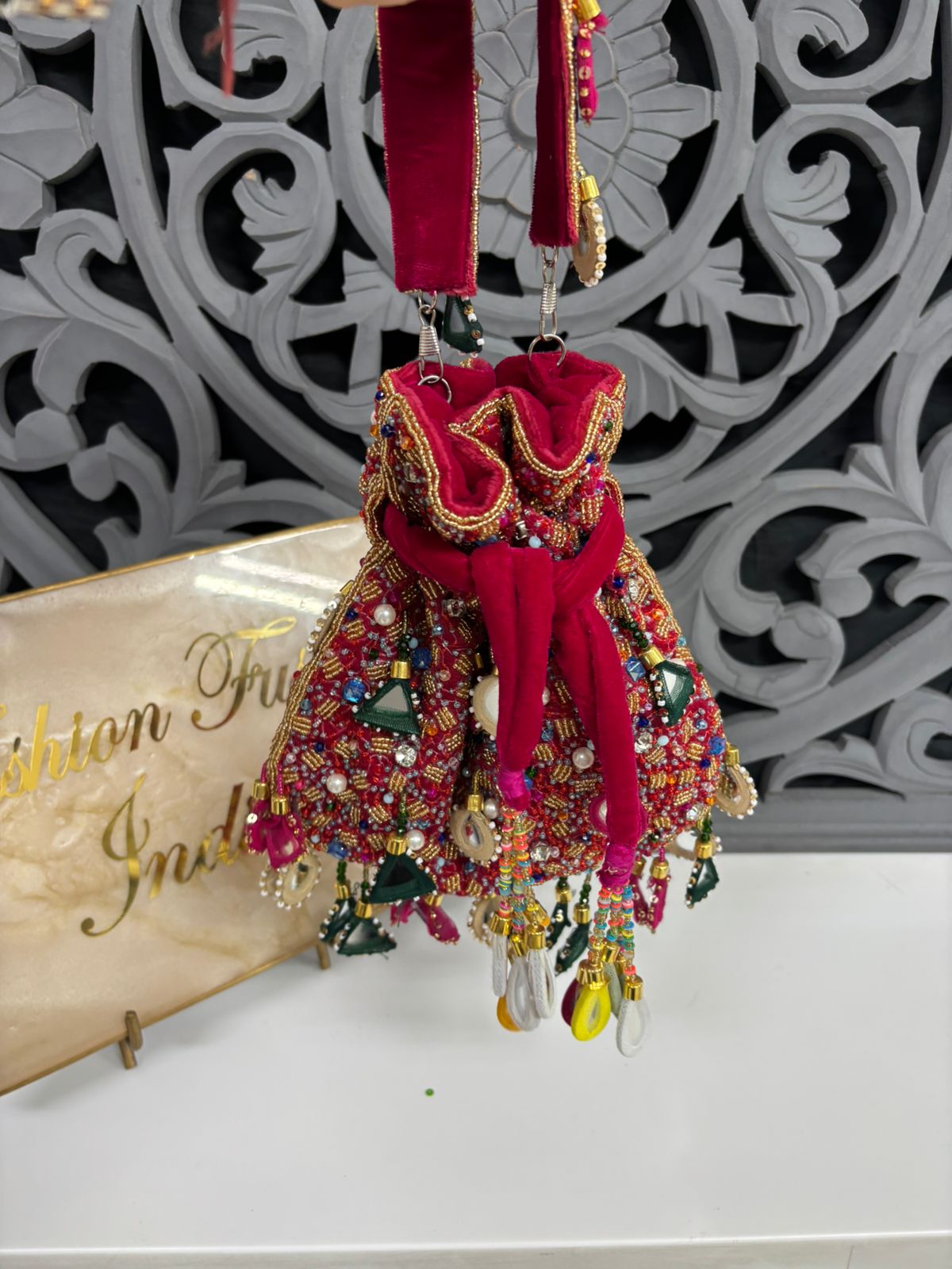 Decorative keychain with colorful beads and red fabric on a white surface with a decorative wall in the background.