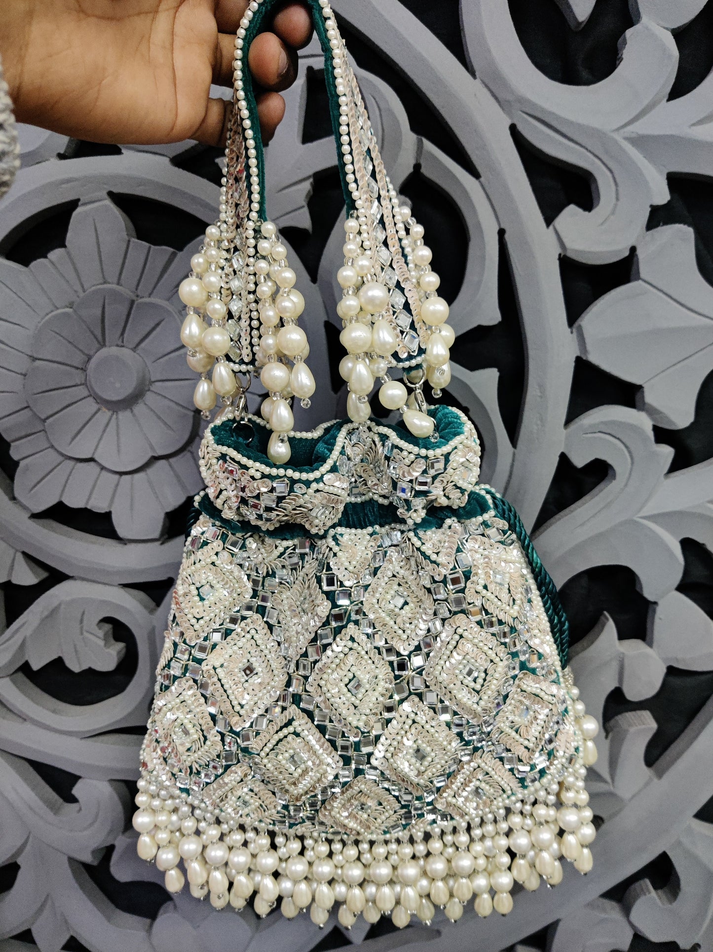 Decorative handbag with pearl embellishments held by a hand against an ornate background