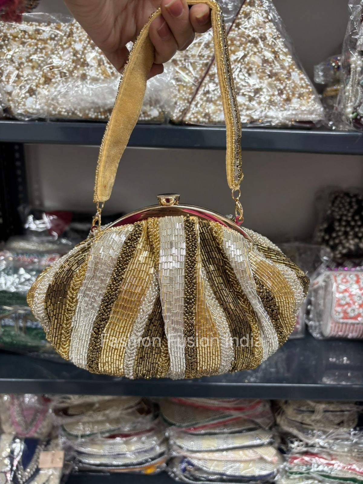 Gold and silver striped handbag held above a store shelf with various items.