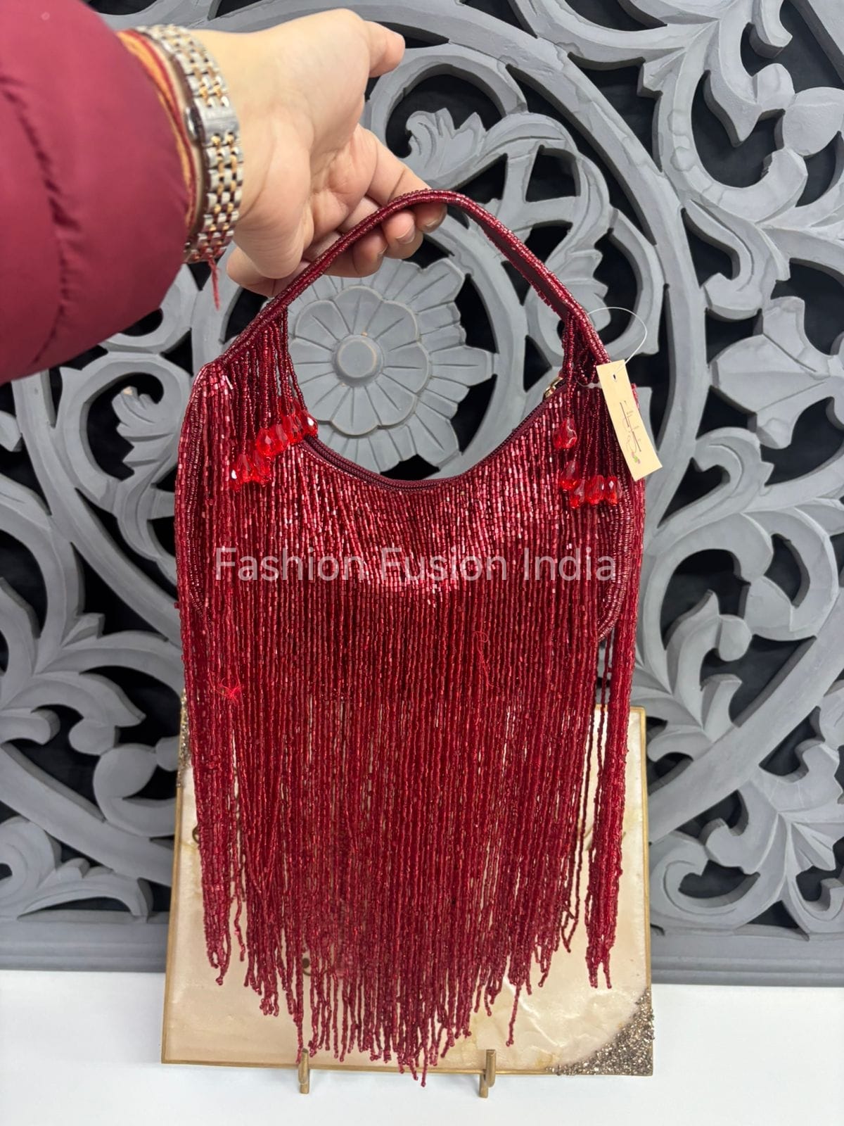 Red fringe handbag held by a hand against a decorative wall.