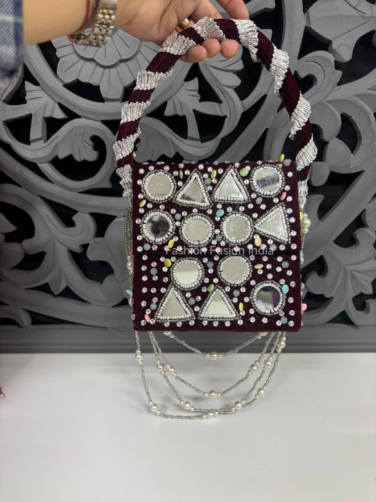 Decorative handbag with geometric patterns and beaded handle against a decorative wall.