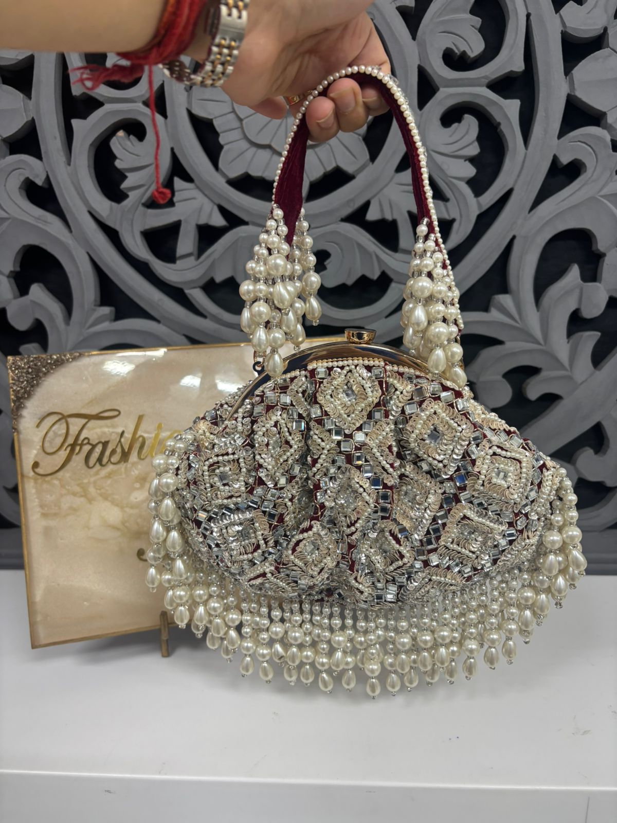 Decorative handbag with pearls and crystals held by a hand against a decorative background.
