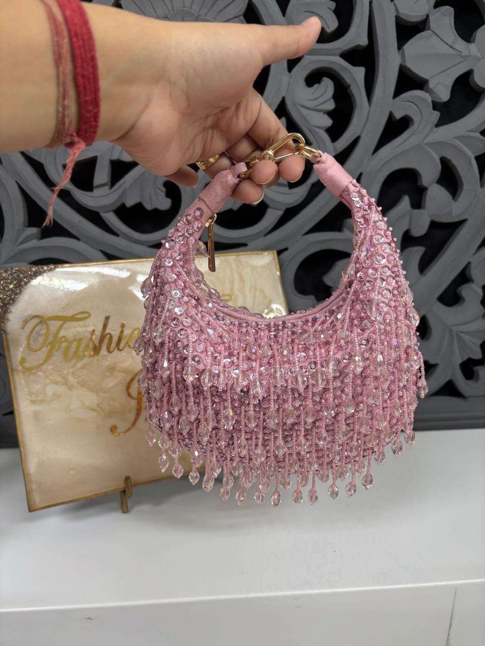 Pink beaded handbag held by a hand with a decorative background