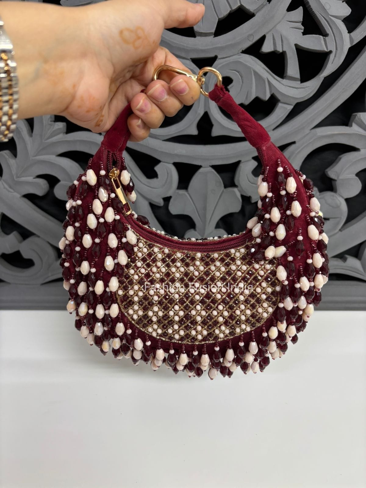 Handbag with decorative beads held by a hand against a decorative wall.