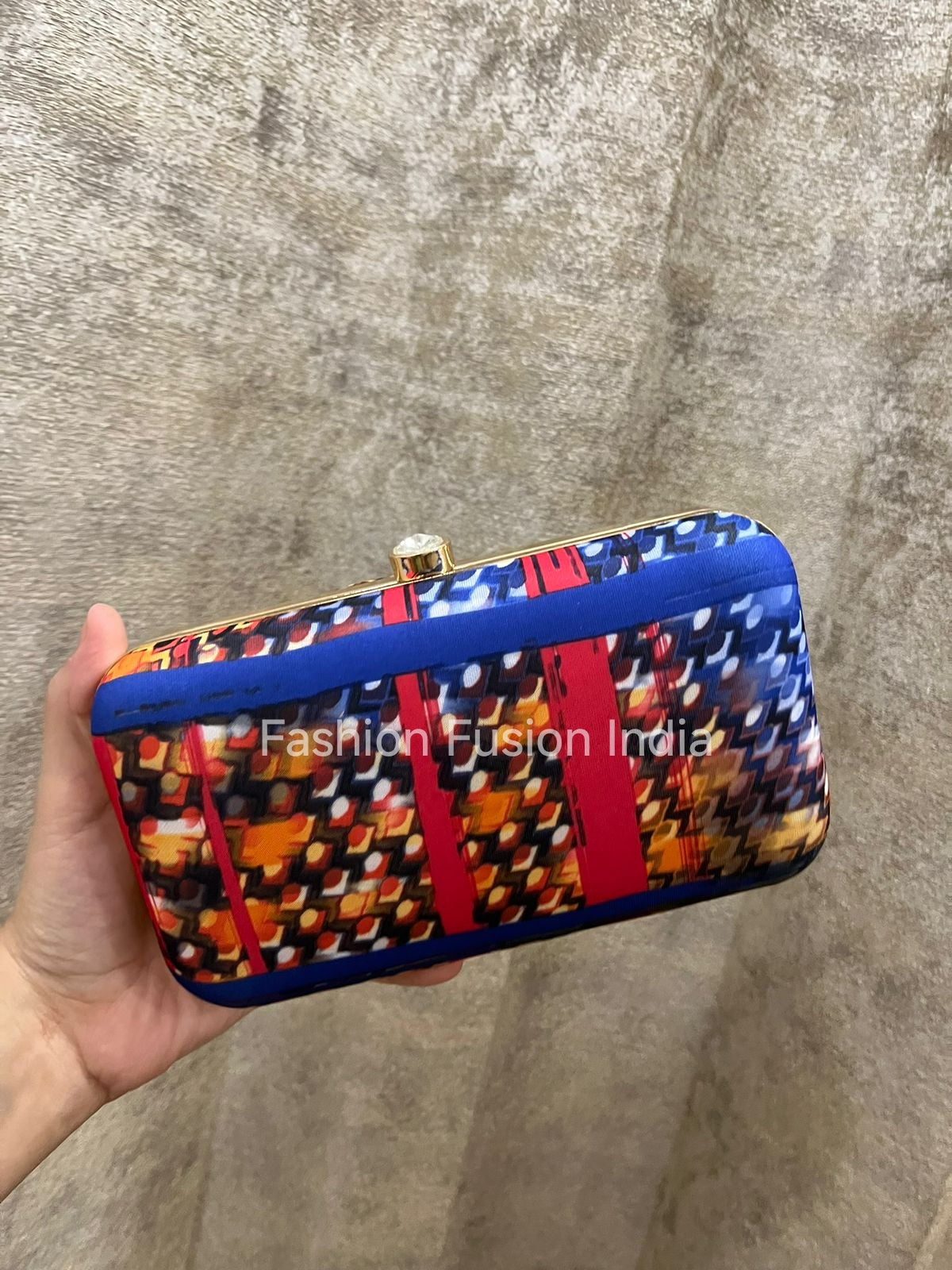 Colorful clutch bag with geometric pattern held by a hand against a textured gray background.
