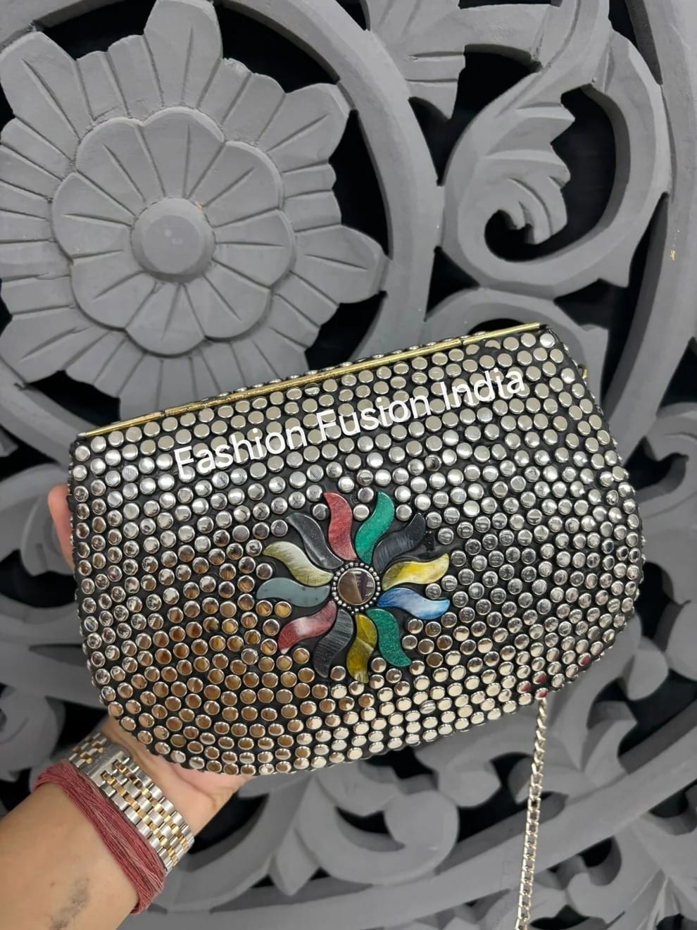 Decorative clutch with floral design and 'Fashion Fusion India' branding against a decorative background.