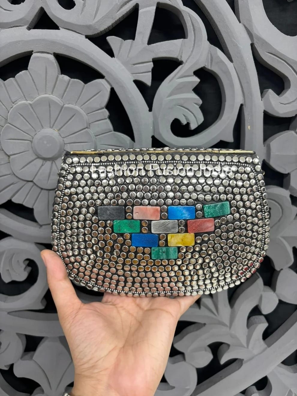 Handheld clutch with colorful geometric pattern against a decorative gray background
