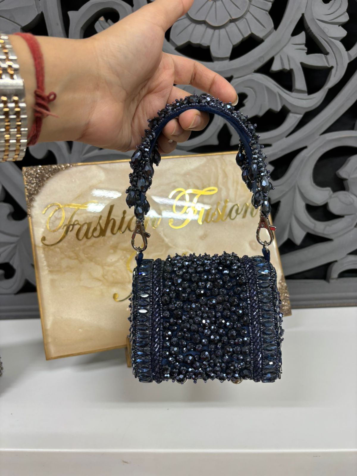 Hand holding a navy blue beaded handbag with 'Fashion Fusion' box in the background