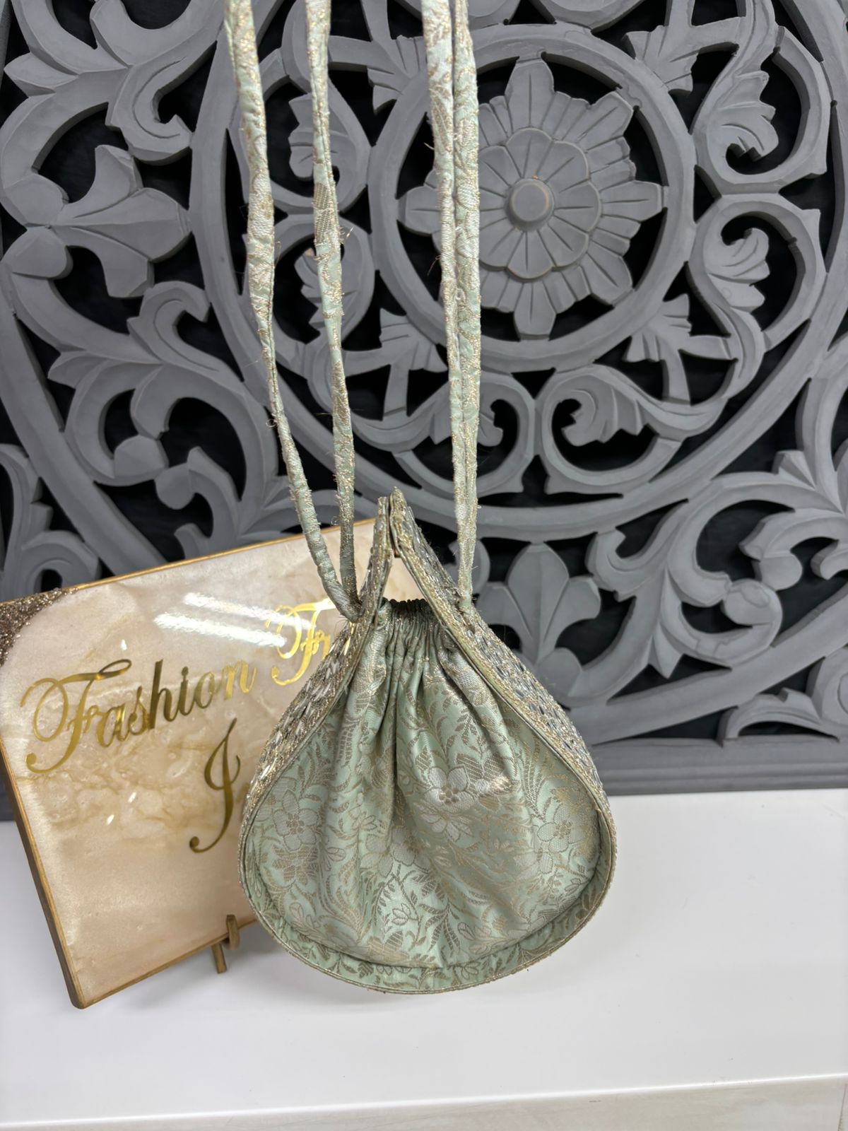 Green drawstring bag on a white surface with decorative background