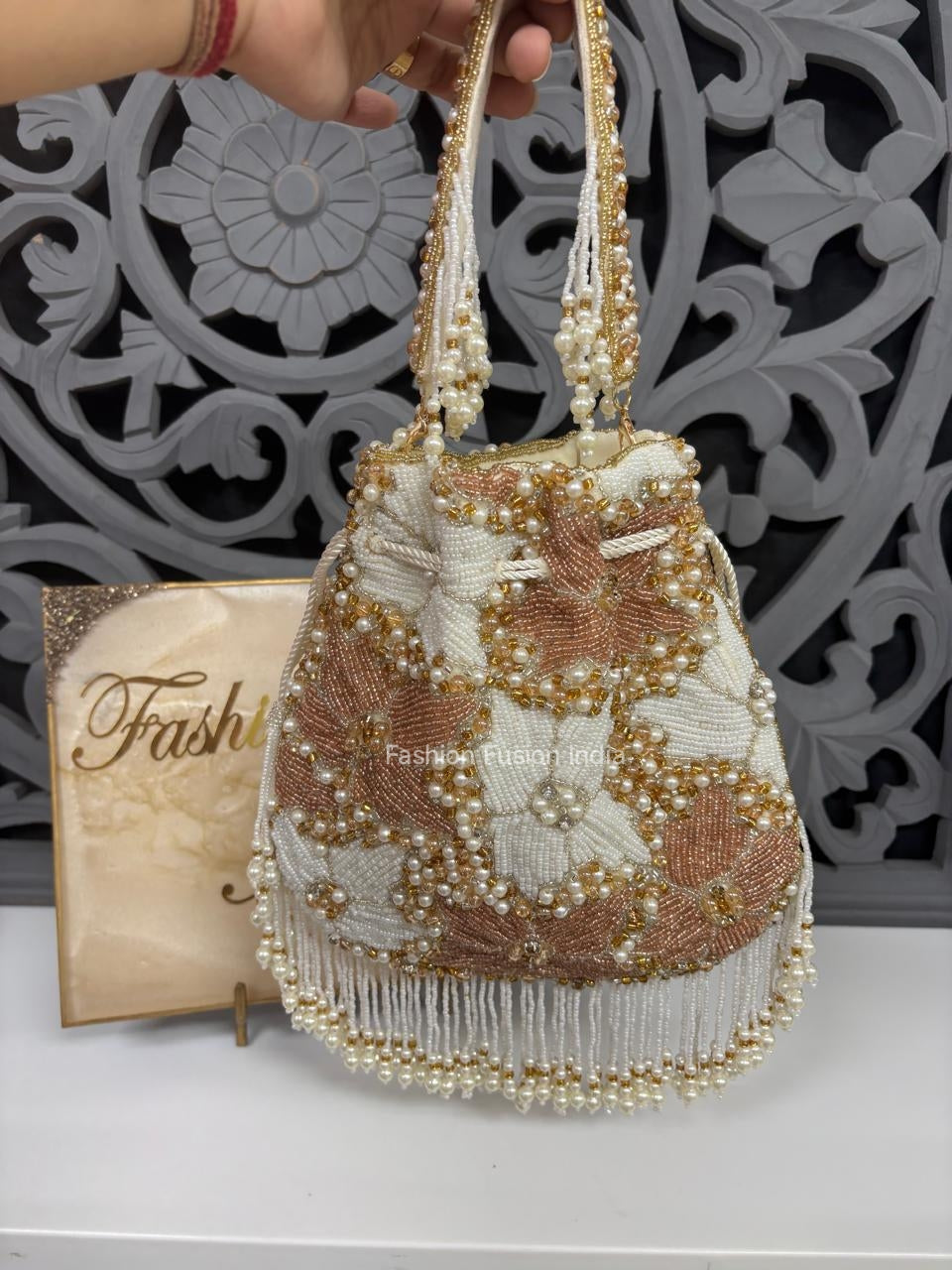 Decorative handbag with beaded details held by a hand against a decorative wall.