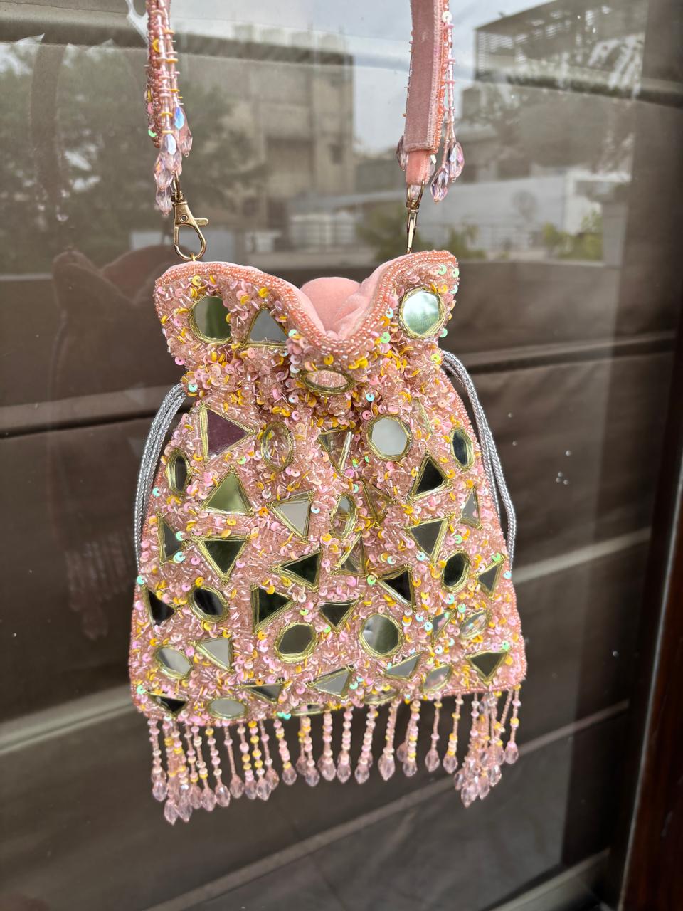 Decorative handbag with beaded design and pink strap on a reflective surface