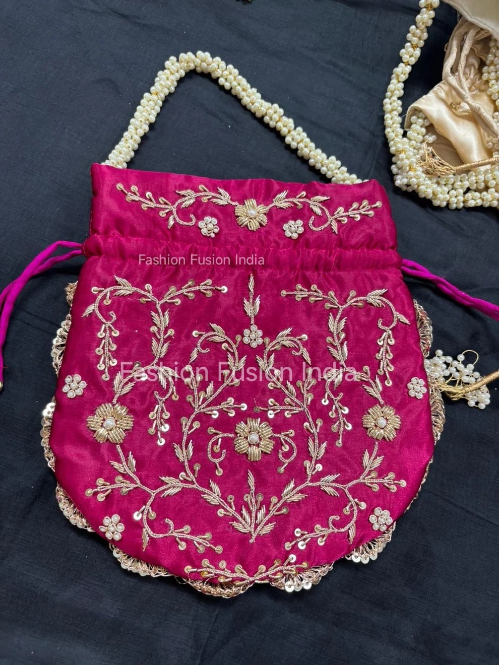 Pink embroidered handbag with gold detailing on a dark background