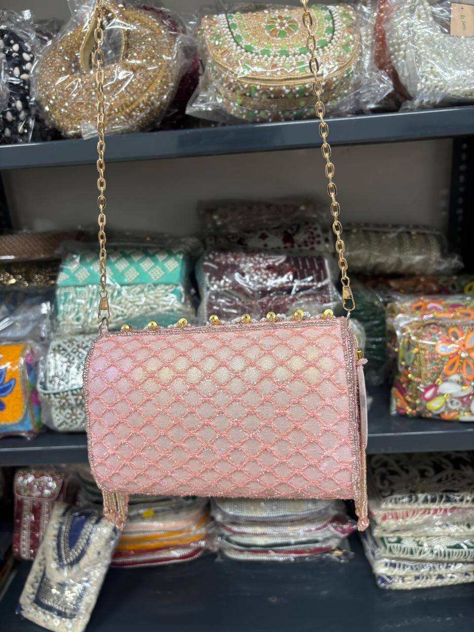 Pink handbag with gold chain on a shelf with other bags in the background