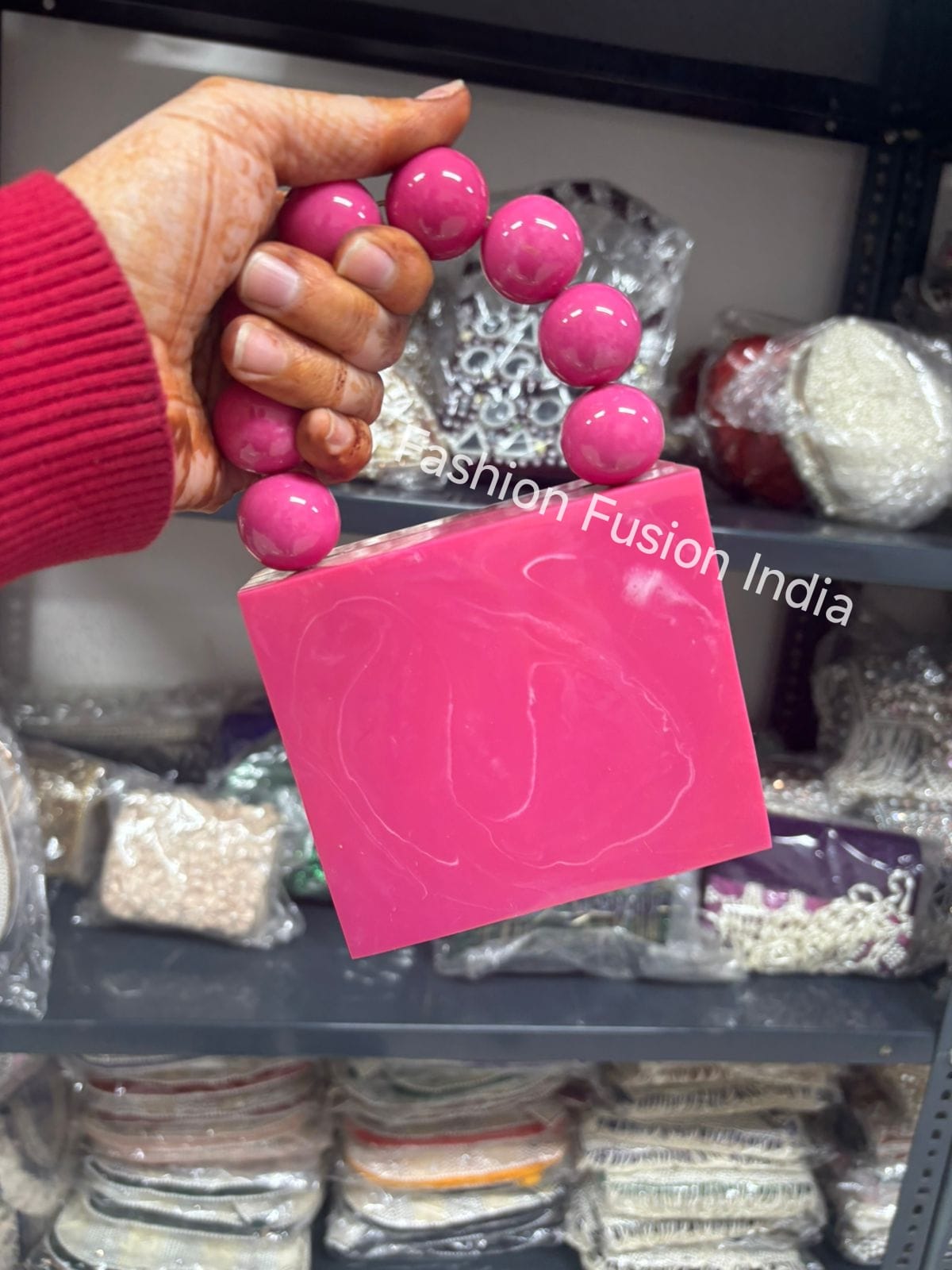 Hand holding pink beads with a 'Fashion Fusion India' sign in a store setting