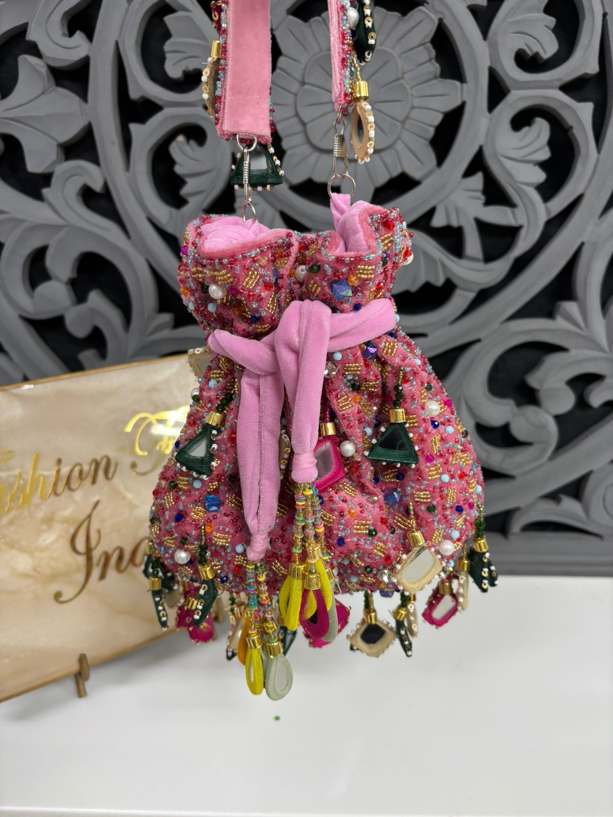 Decorative pink dress ornament with beads and ribbons on a white surface with a decorative gray background.