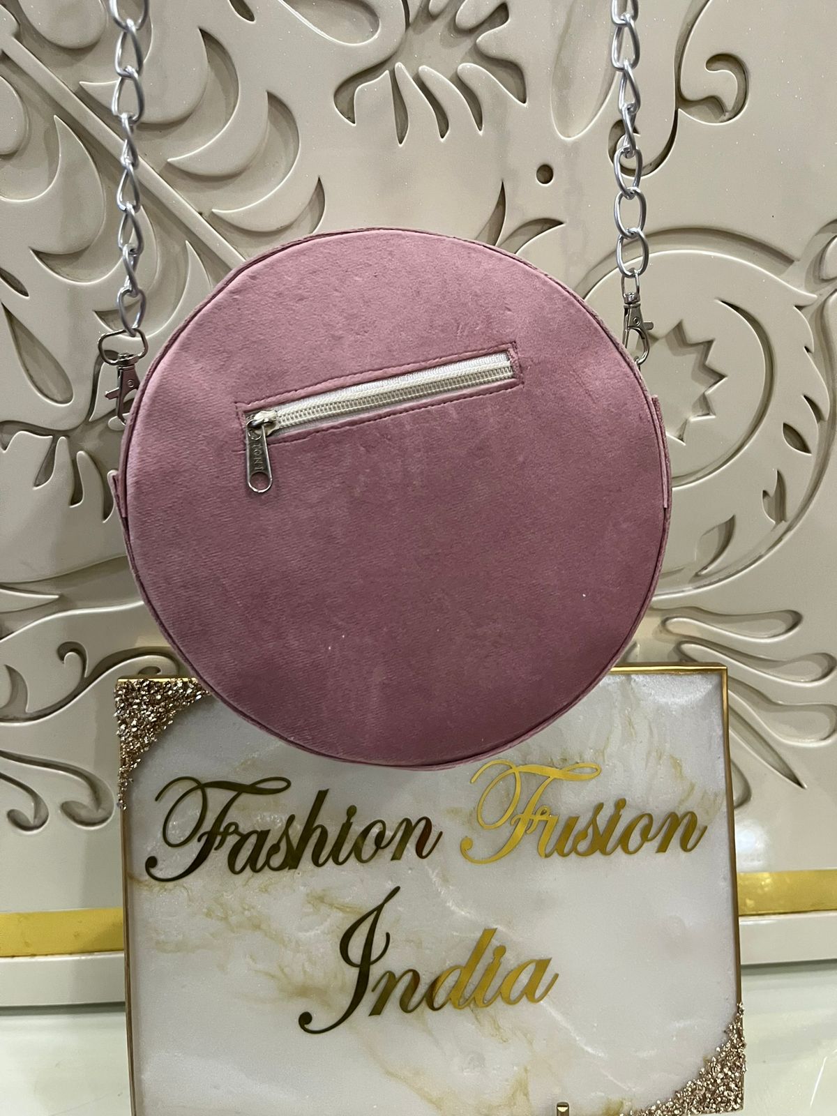 Pink round handbag with a chain strap on a decorative background with 'Fashion Fusion India' branding.