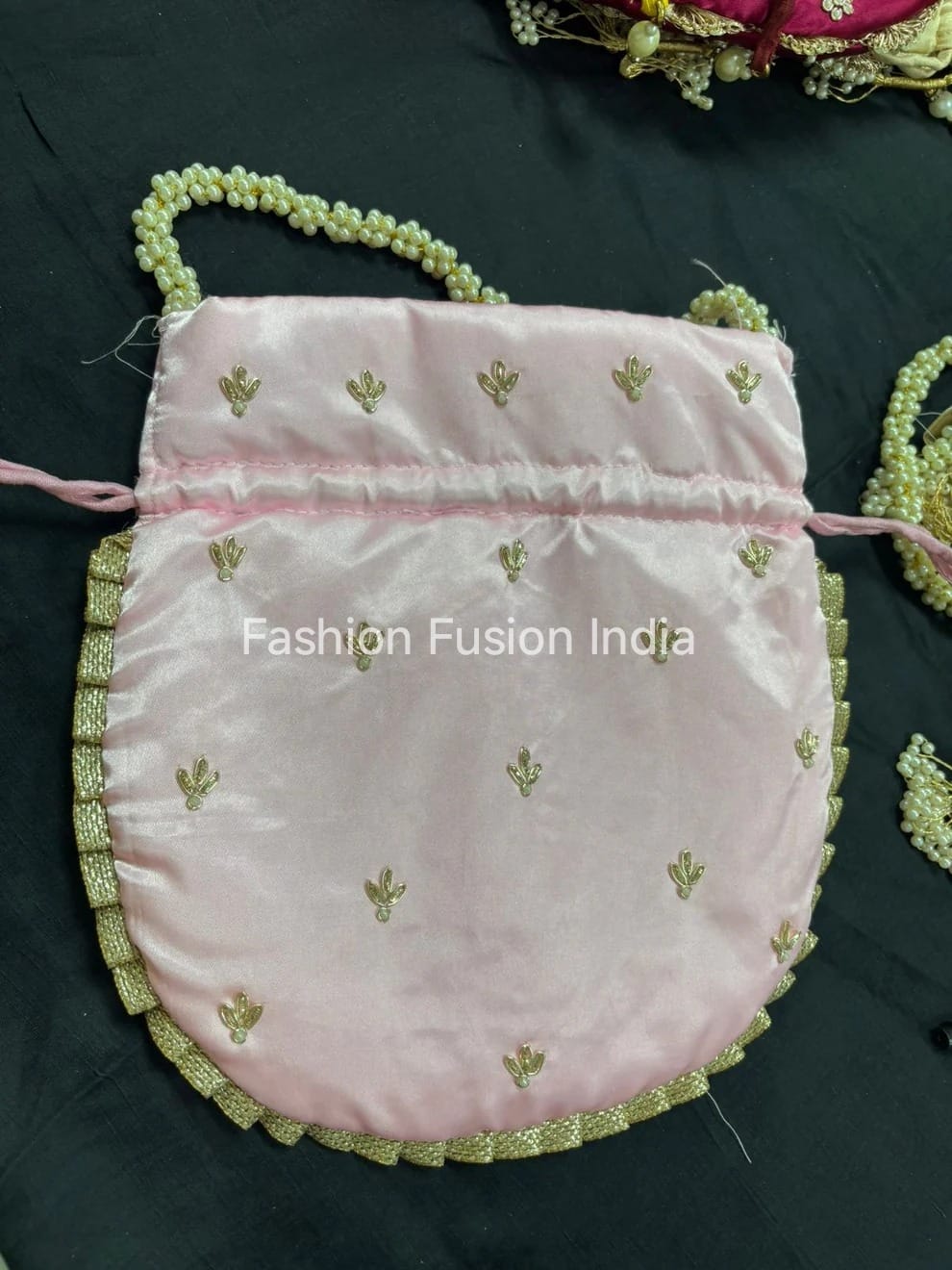 Pink drawstring bag with gold embroidery on a black background, branded 'Fashion Fusion India'.