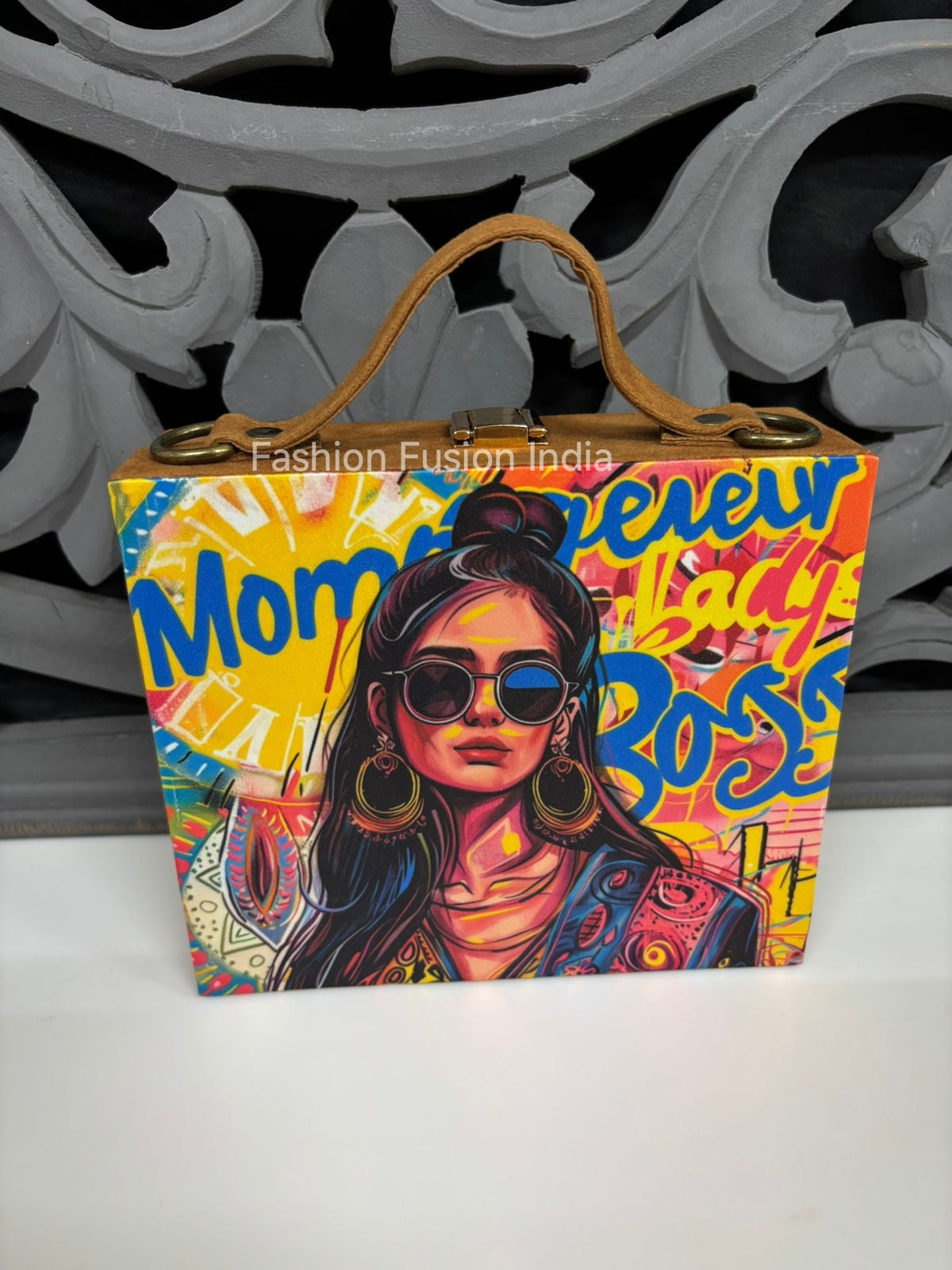 Vibrant graphic print wooden clutch bag with trendy female artwork against carved grey backdrop.