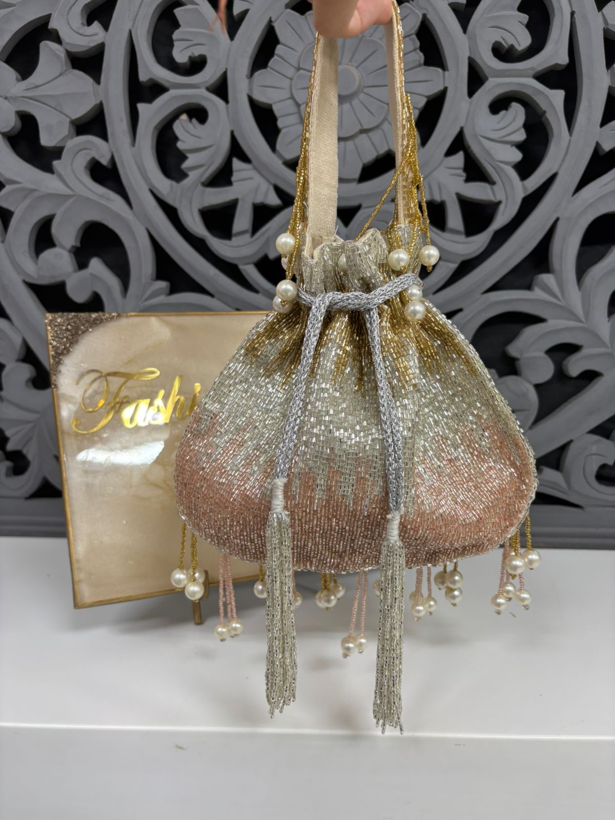 Decorative handbag with tassels and pearls on a white surface with a decorative gray background.