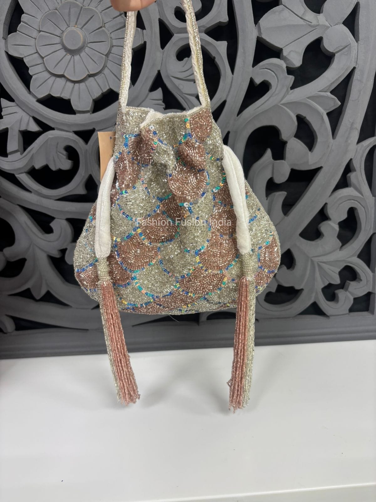 Beaded handbag with tassels held against a decorative gray background