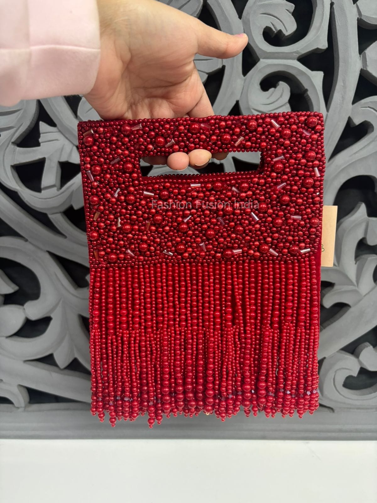 Red beaded clutch held by a hand against a decorative gray background