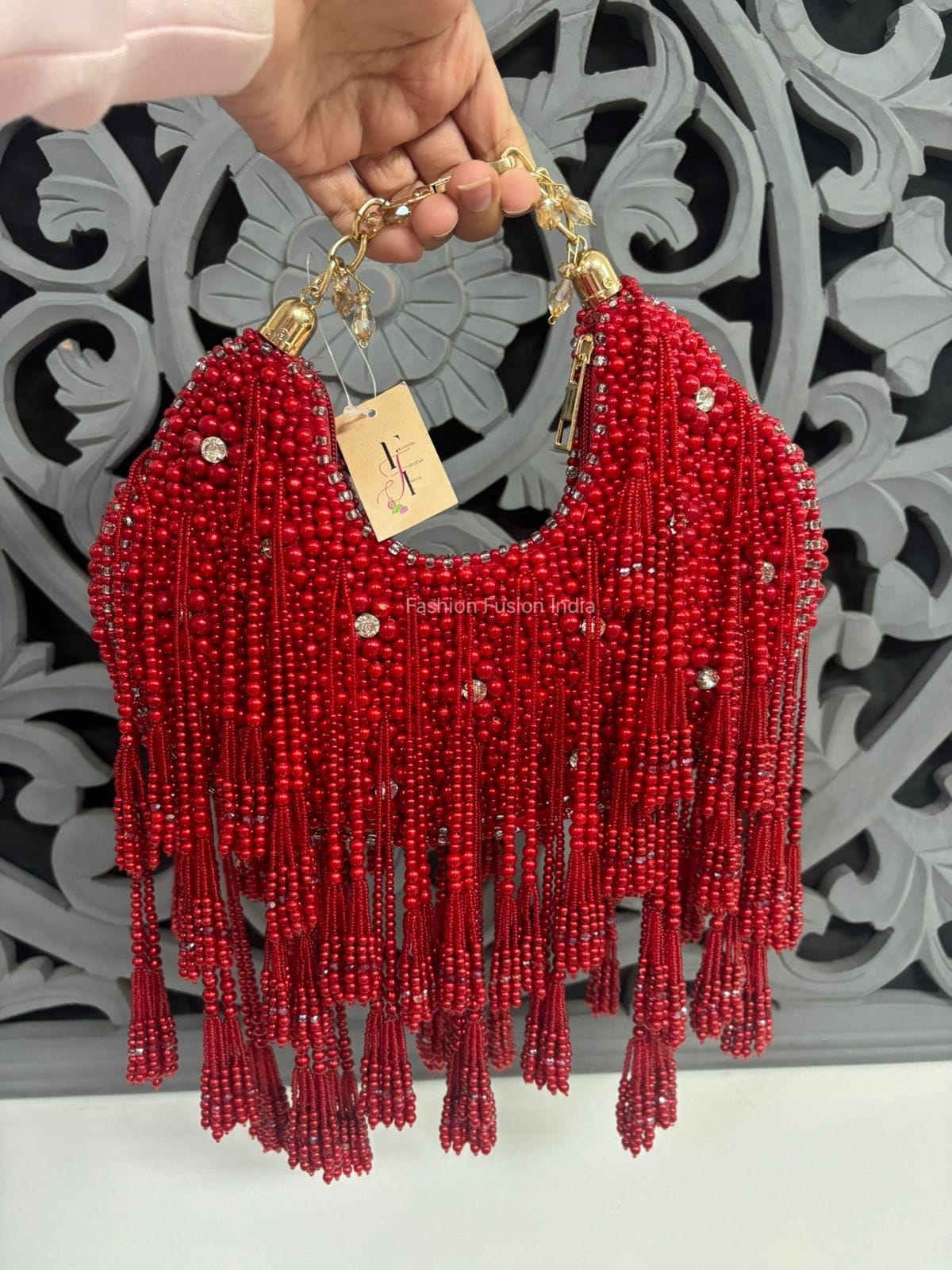 Red beaded handbag with gold accents held by a hand against a decorative background