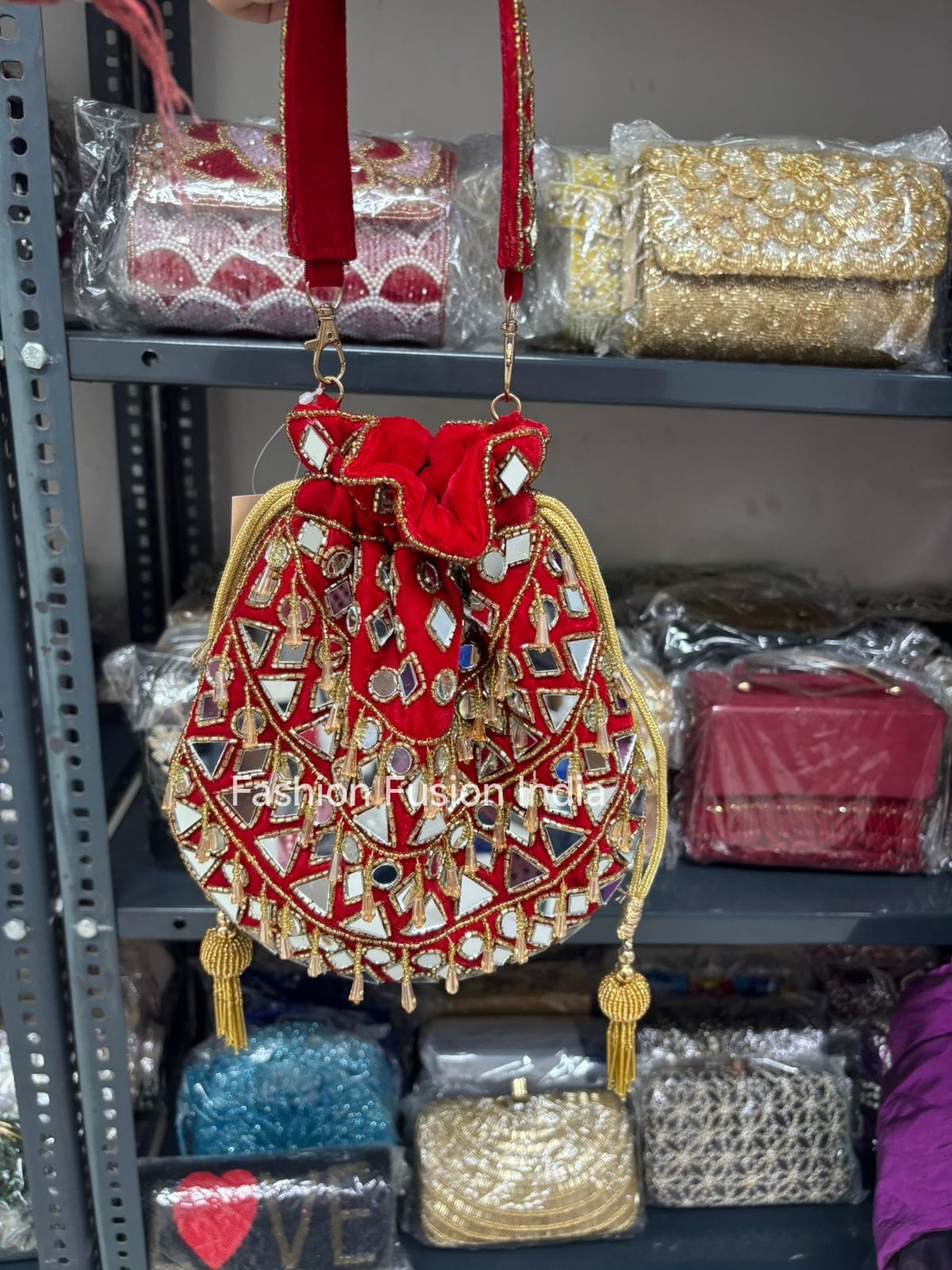 Decorative handbag with red and gold details on a shelf with other bags.