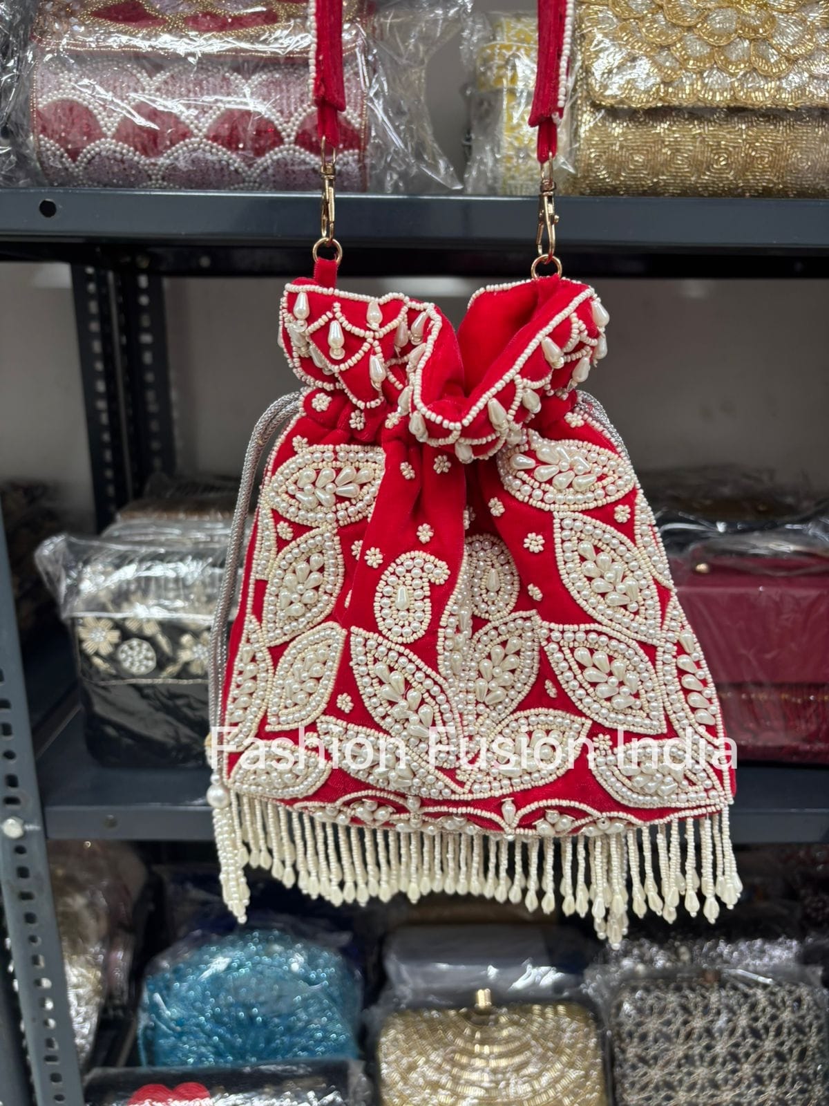 Red and white embroidered handbag with fringes on a shelf with other bags.