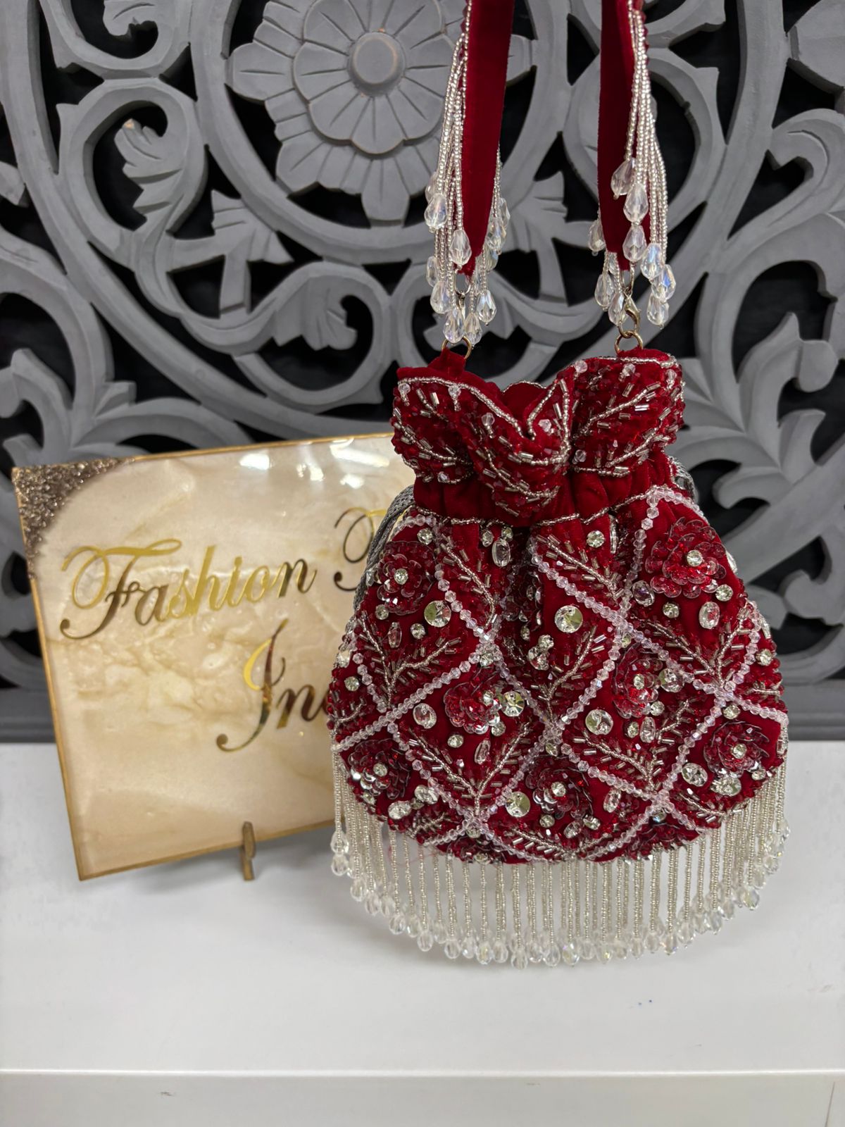 Red beaded handbag with decorative bow on a white surface with a decorative background