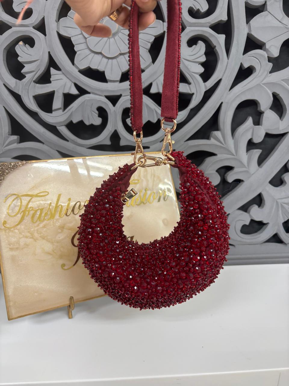 Red beaded handbag with gold accents held by a hand against a decorative wall.