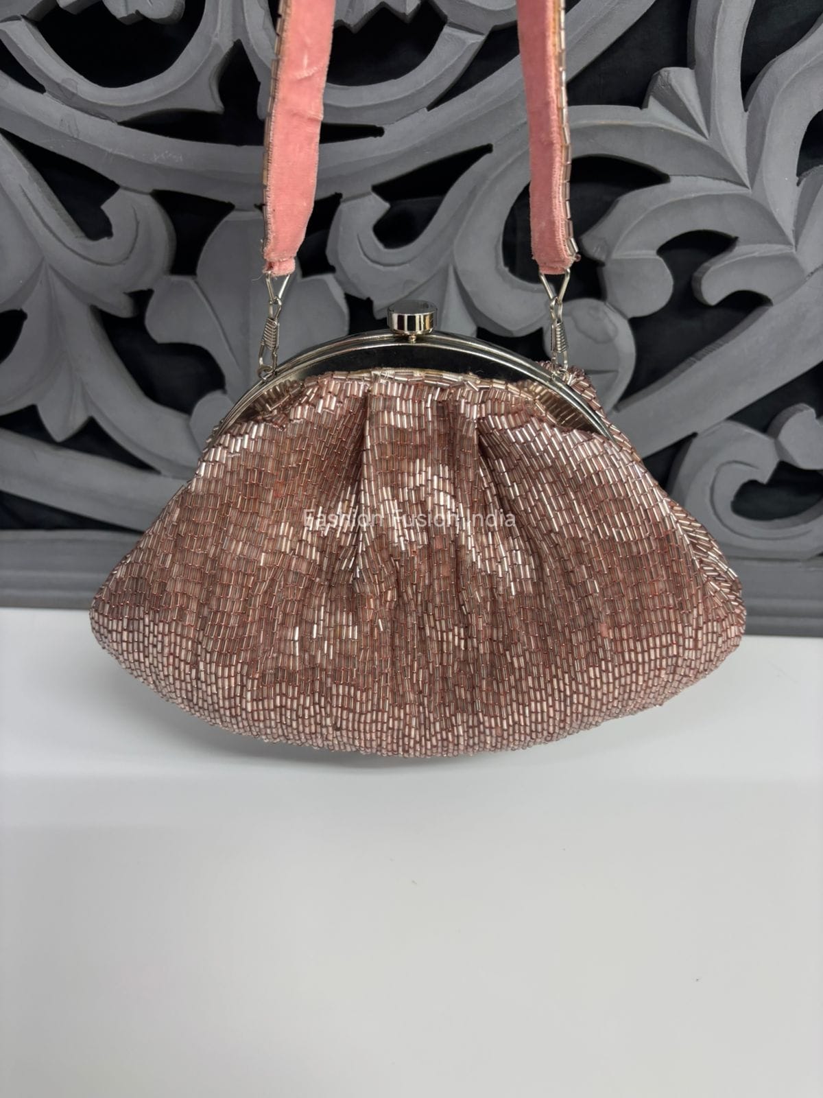 Metallic Batua bag with pink strap on a white surface with decorative gray background