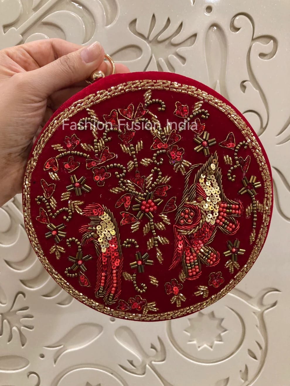 Red embroidered round clutch held by a hand on a decorative background