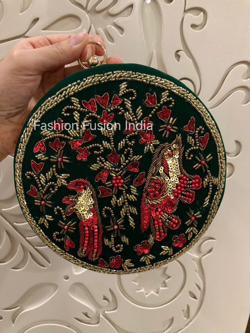 Round embroidered clutch with parrot design held by a hand against a decorative white background.