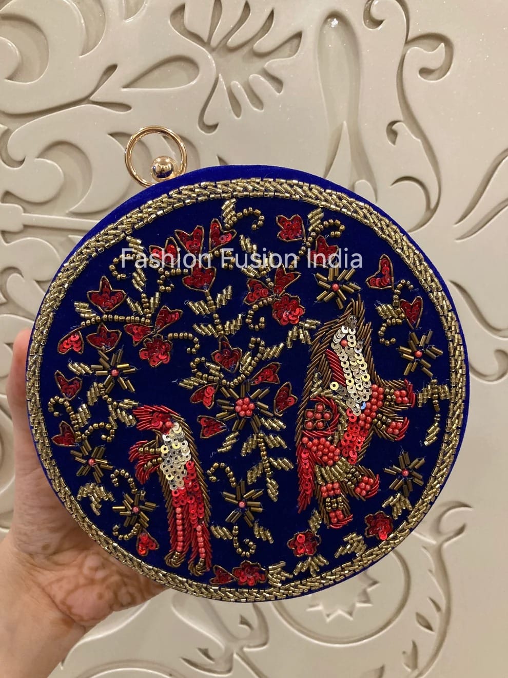 Round embroidered clutch with birds and floral patterns held against a decorative white background.