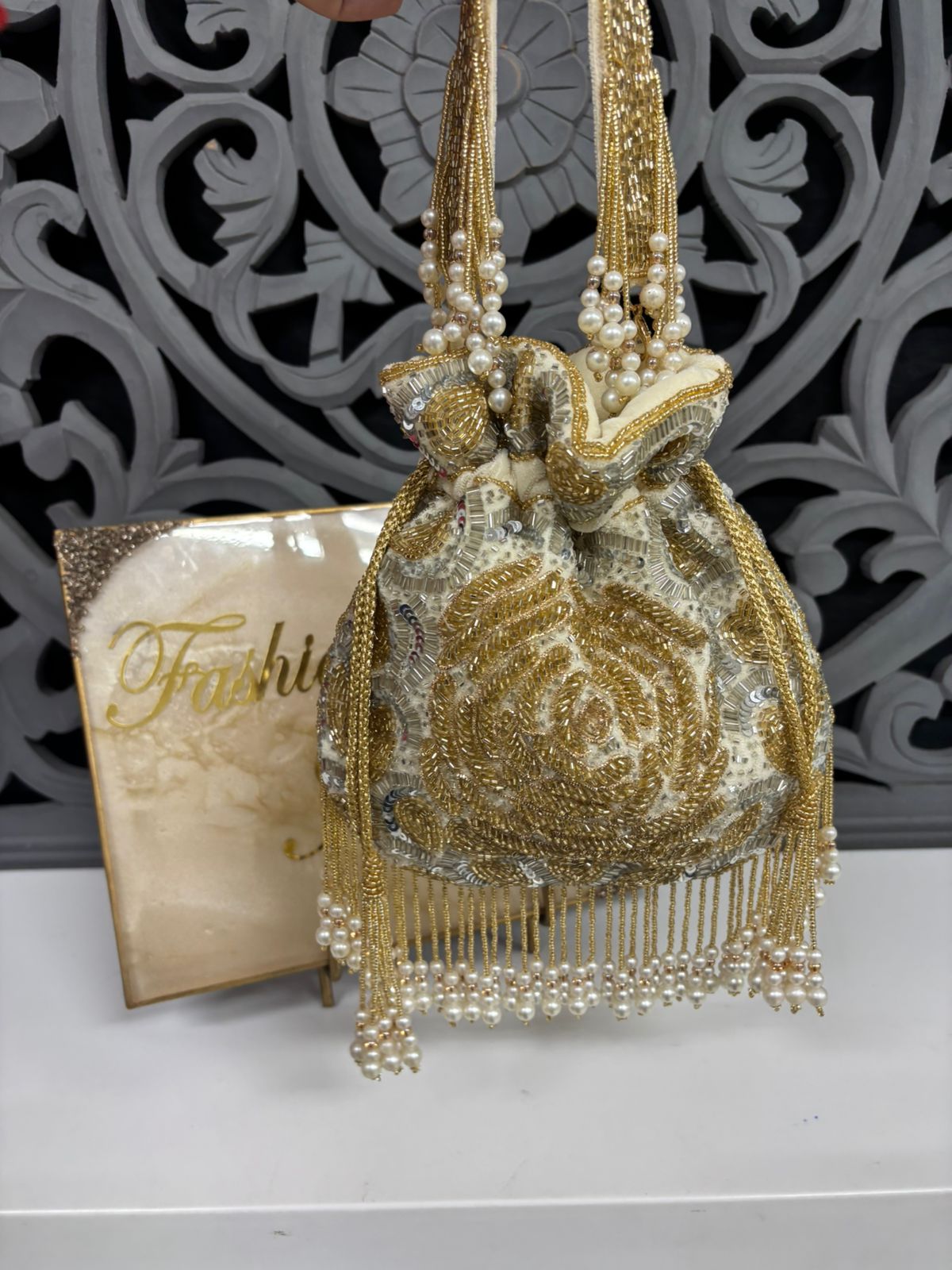 Gold beaded handbag with pearl details on a decorative background