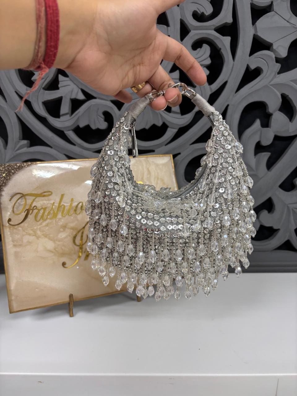 Silver beaded handbag held by a hand with a decorative background