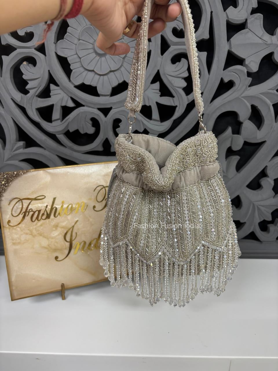 Silver beaded handbag held by a hand with a decorative background