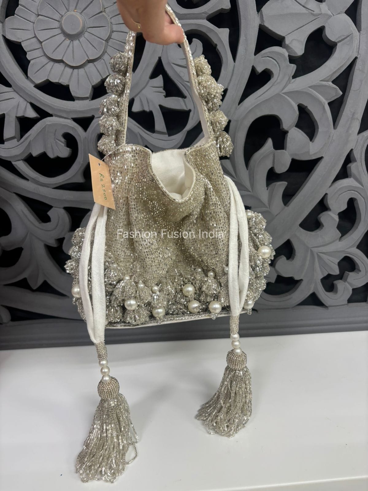 Decorative handbag with tassels and beads held against an ornate wall.