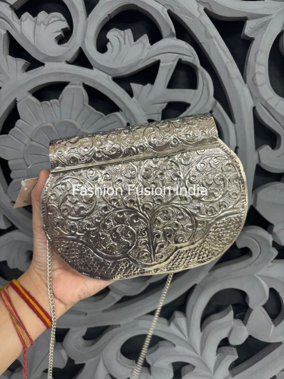 Silver embossed clutch held by a hand against an ornate decorative background with 'Fashion Fusion India' branding.