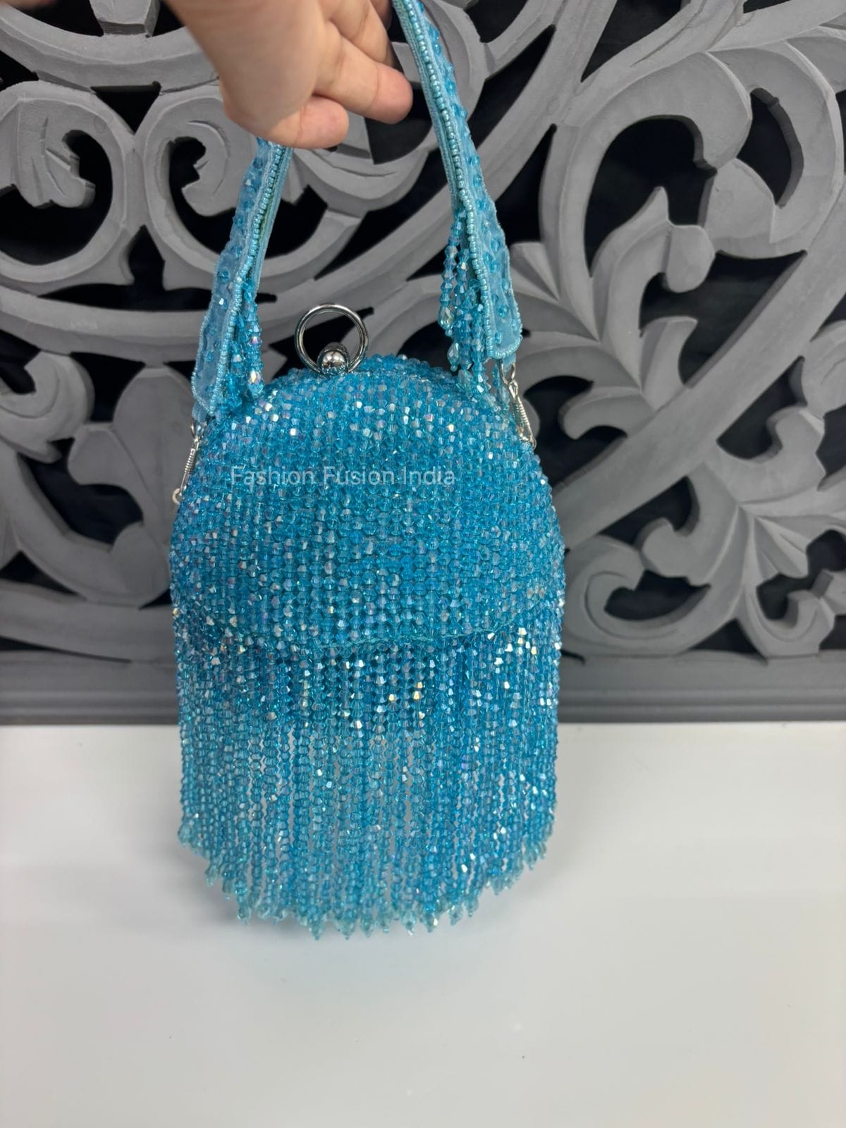 Blue beaded handbag held by a hand against a decorative wall.