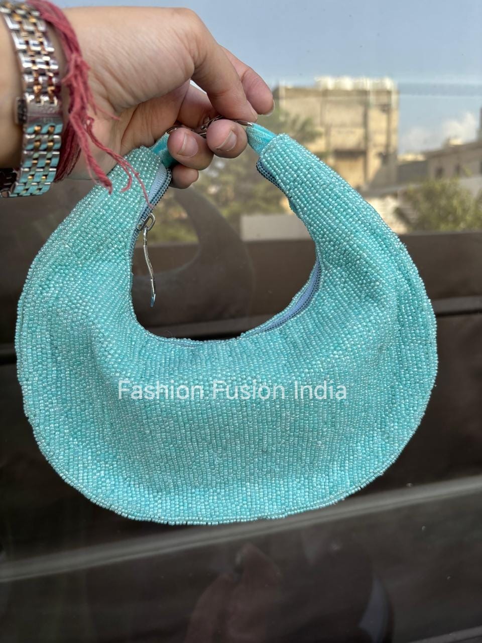Turquoise handbag held by a hand with a blurred background
