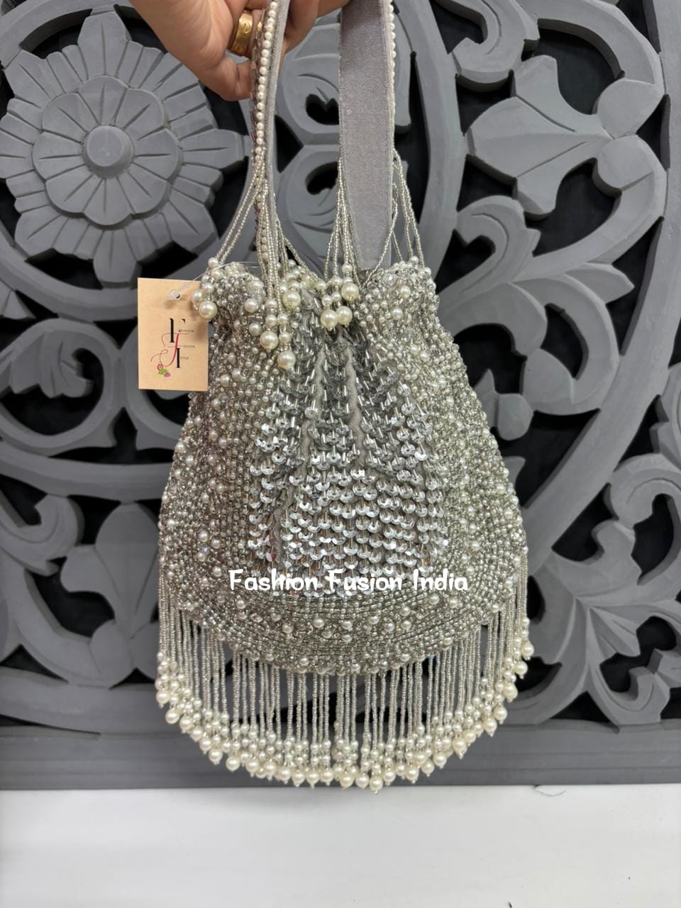 Silver beaded handbag with decorative elements against a decorative wall.