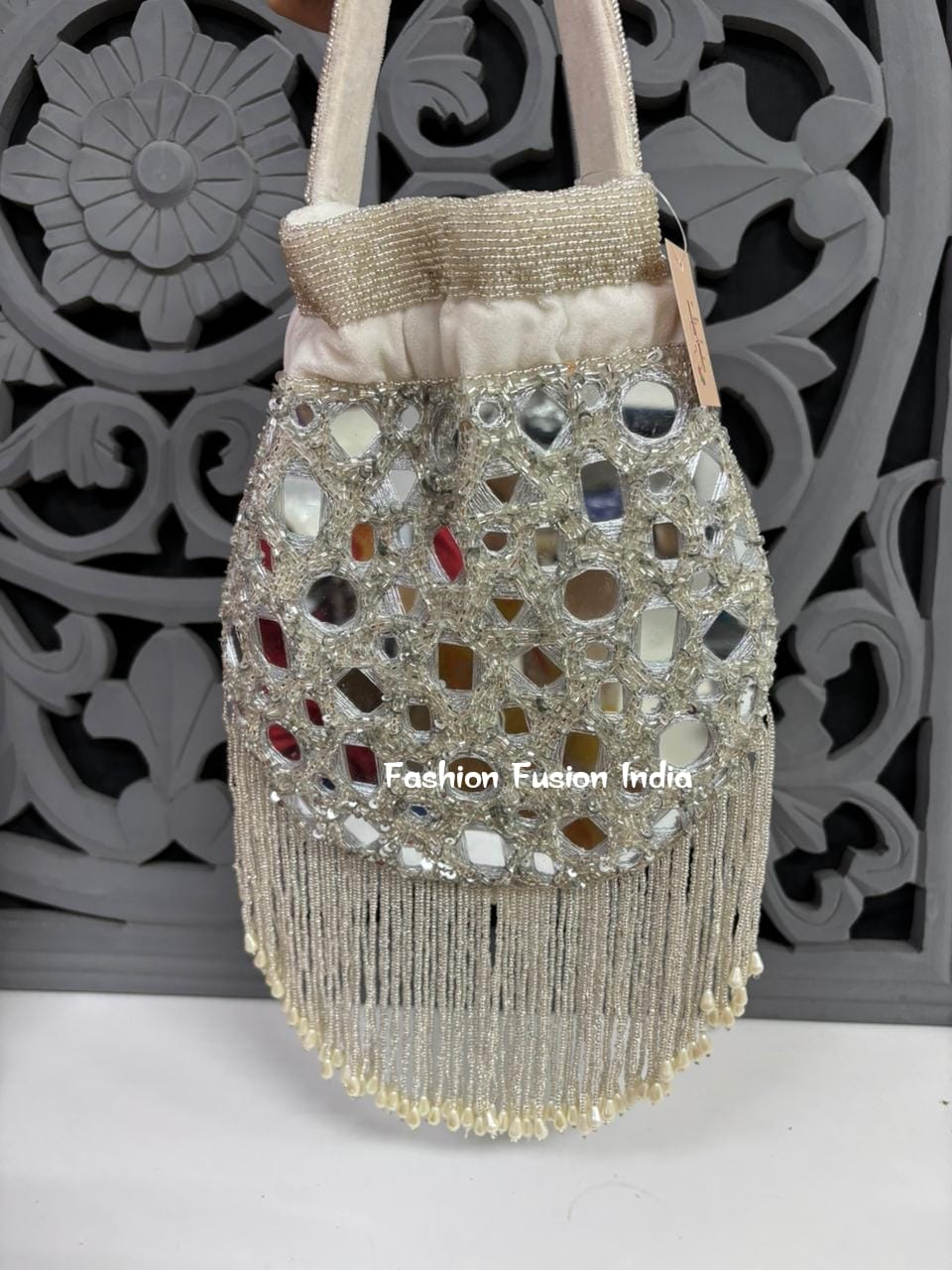 Decorative handbag with mirror embellishments and fringes against a decorative gray background.