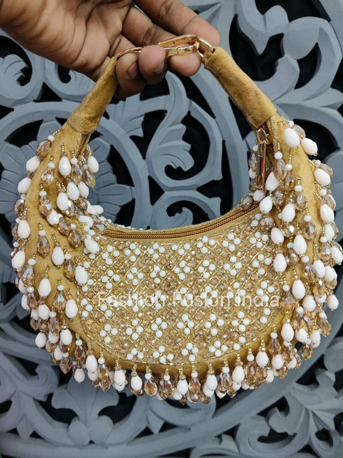 Gold handbag with white bead embellishments held by a hand against a decorative background.