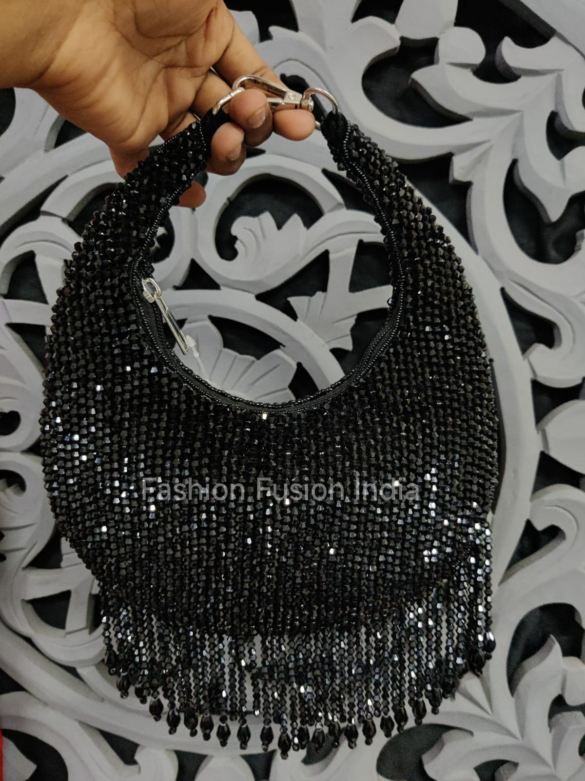 Black beaded handbag held by a hand against a decorative black and white background.