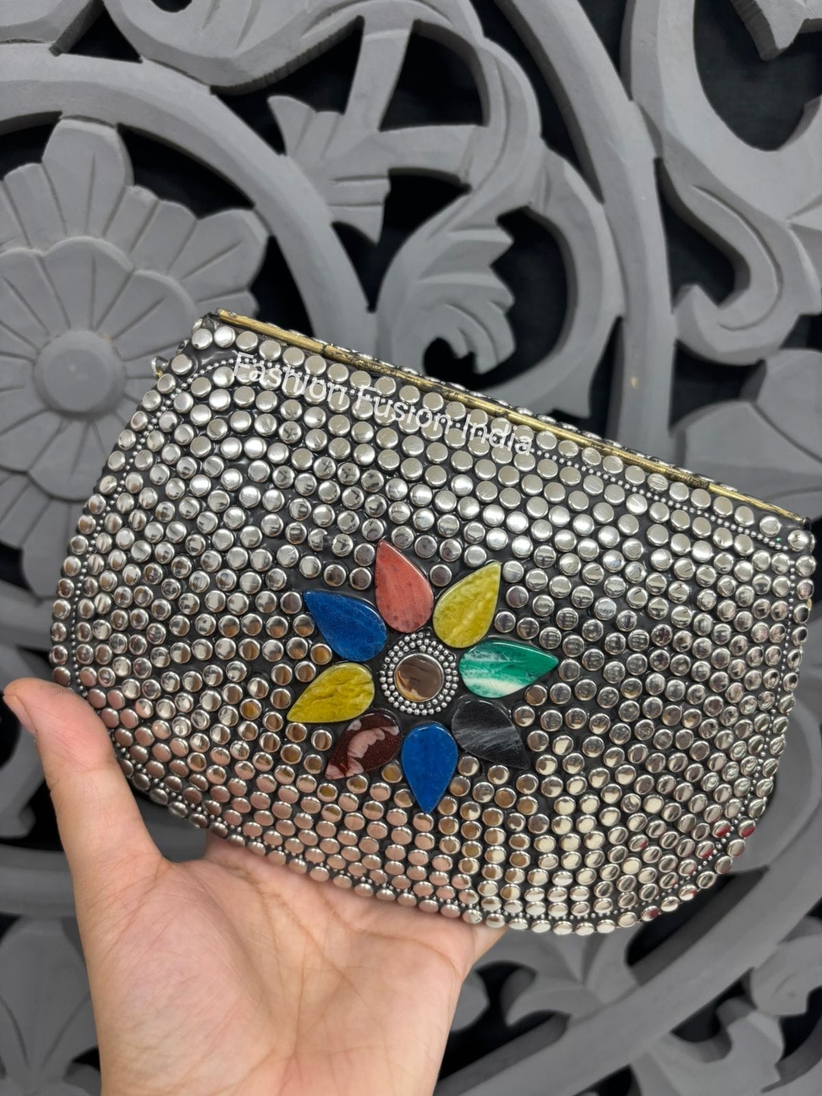 Silver studded clutch with a colorful flower design held against a decorative gray background
