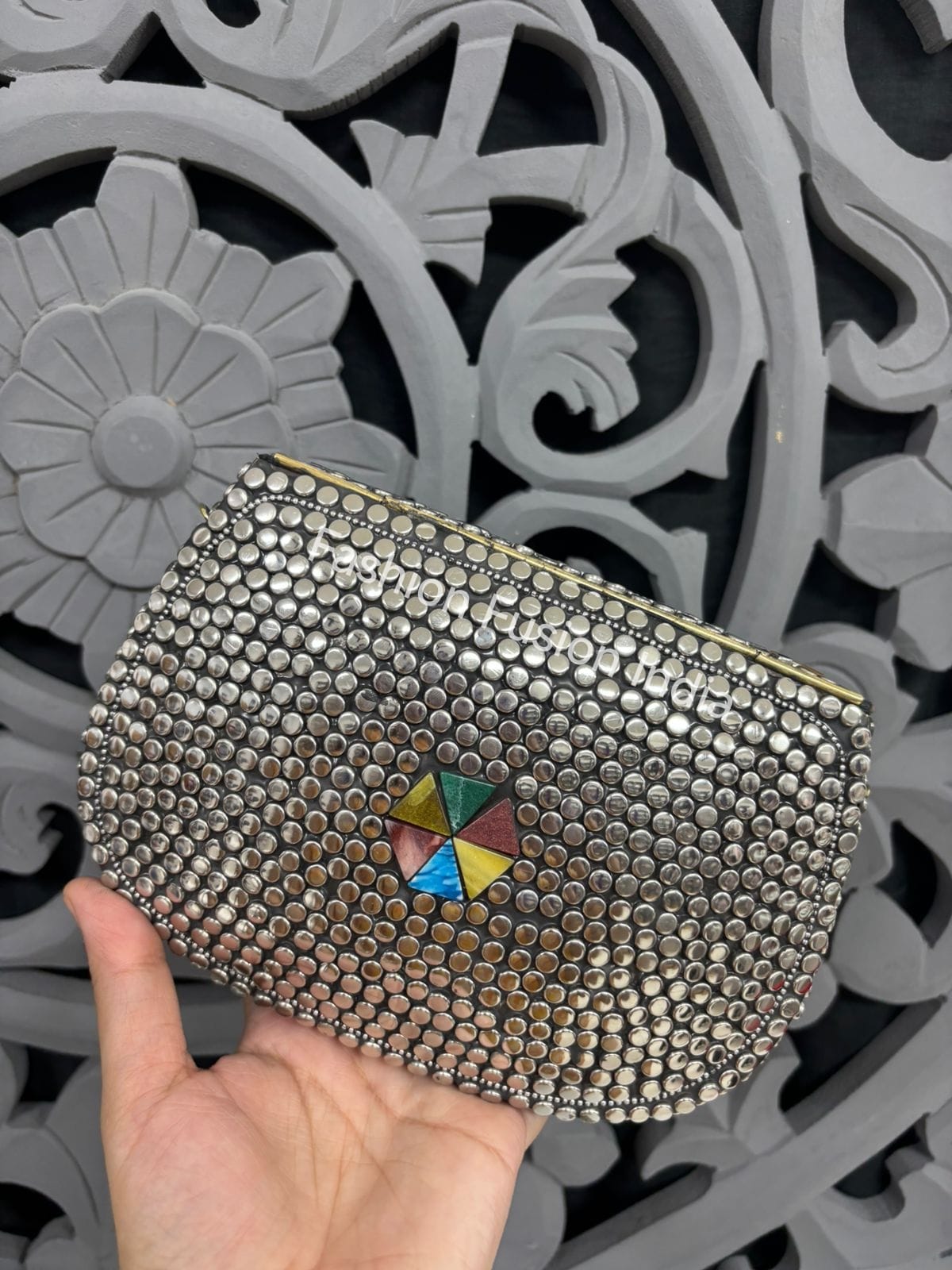 Silver studded clutch with a colorful center held against a decorative gray background