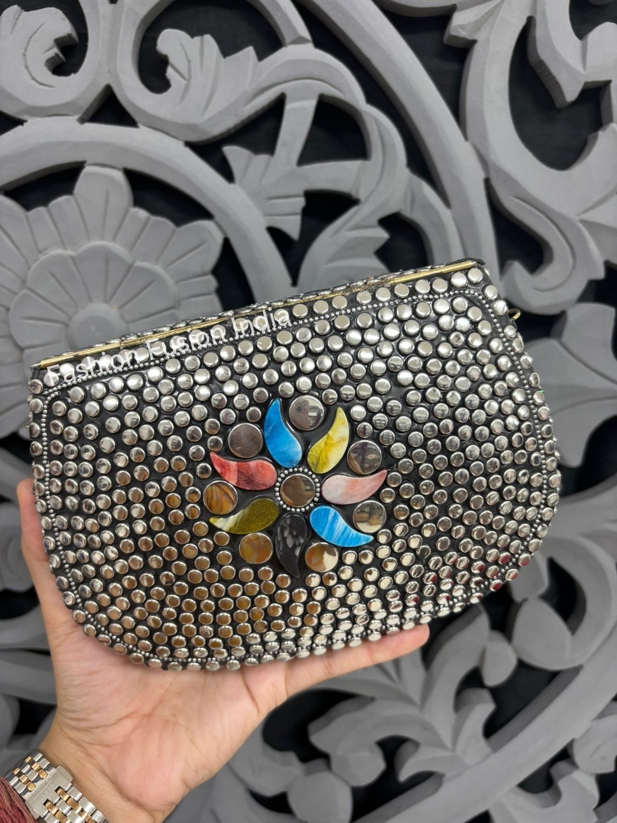 Decorative clutch with floral design held by a hand against an ornate gray background
