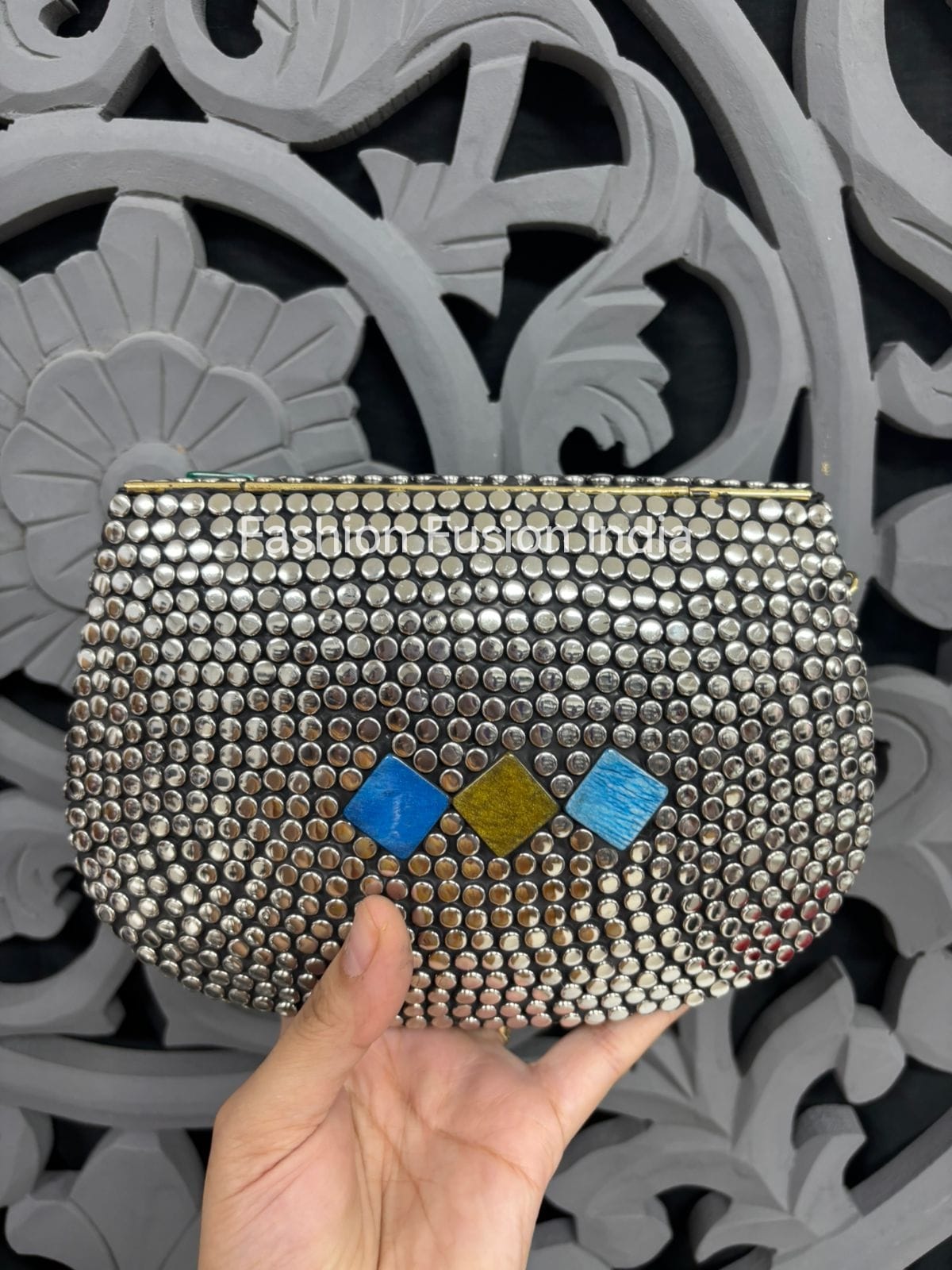 Silver studded clutch with colorful accents held against a decorative gray background